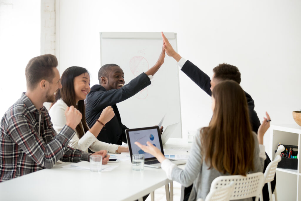 Excited diverse executive colleagues or partners giving high five at team meeting, happy smiling multiracial businessmen celebrating good teamwork result motivated by great achievement or victory