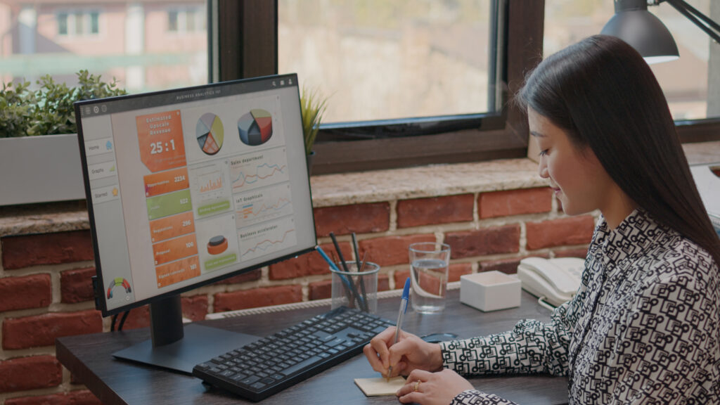 Person writing on sticky notes to remember task on computer. Business woman using post it memo paper as reminder to work on project planning for company efficiency and inspiration.
